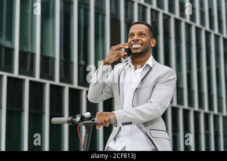 Élégant homme d'affaires afro-américain gai à cheval et à parler téléphone mobile dans le centre-ville Banque D'Images