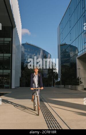 Ravie femme entrepreneur souriant et à vélo par beau temps dans le centre-ville de la ville moderne Banque D'Images