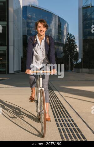 Ravie femme entrepreneur souriant et à vélo par beau temps dans le centre-ville de la ville moderne Banque D'Images