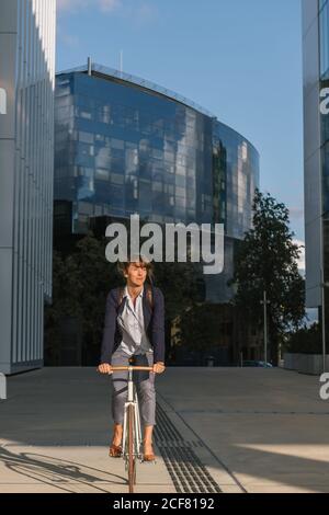 Ravie femme entrepreneur souriant et à vélo par beau temps dans le centre-ville de la ville moderne Banque D'Images