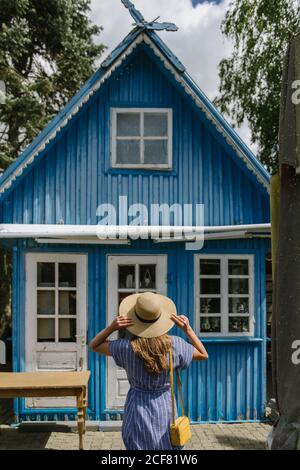Vue arrière de la femme en chapeau de paille et de la sundress debout devant la maison d'été bleu coloré en plein jour Banque D'Images