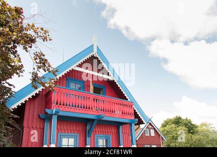 Extérieur lumineux de maison en bois avec toit de pignon et vibrant des éléments rouges et bleus dans la campagne verte le jour ensoleillé Banque D'Images