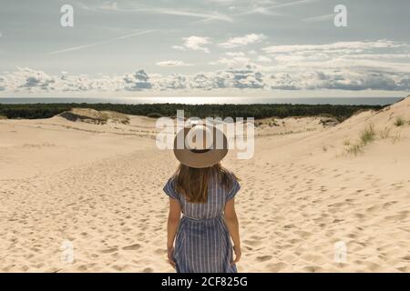 Femme adulte en robe décontractée et chapeau de paille debout sur une dune de sable le jour chaud d'été Banque D'Images