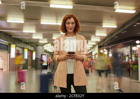 Jeune femme aux cheveux rouges utilisant un smartphone à la station Banque D'Images