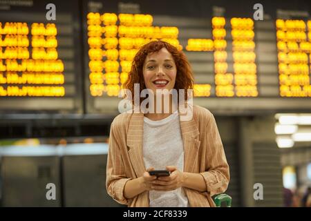 Jeune femme aux cheveux rouges utilisant un smartphone à la station Banque D'Images