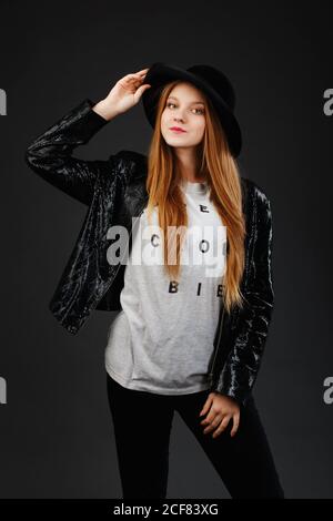 Portrait de la belle jeune fille portant chapeau en feutre noir et veste en cuir sur fond gris foncé Banque D'Images