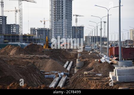 Pose de tuyaux d'égout pluvial souterrains sur le chantier de construction. Installation de conduites d'eau et d'égouts sanitaires sur les grues de fond et les grues bleues Banque D'Images