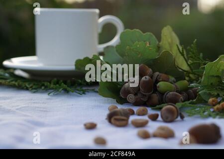 Composition de café avec une tasse de café blanc rôti au milieu grains de café et glands sur la nappe en toile comme arrière-plan Banque D'Images