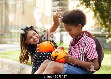 Deux amis avec des sacs sous forme de citrouilles assises plein air et s'amuser Banque D'Images