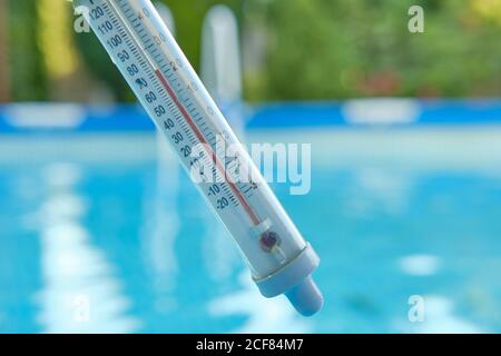 Thermomètre mesurant la température de l'eau pour nager sur un fond flou d'eau bleue dans la piscine. Concept d'été. Banque D'Images