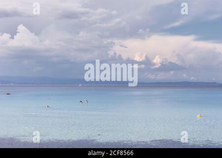 Eau de mer paisible avec des personnes nageant dans un climat calme sous ciel nuageux, Halkidiki, Grèce