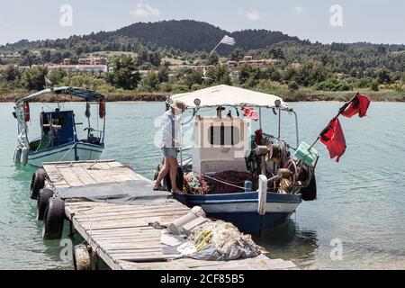 Vue latérale d'une femme mûre qui passe de la jetée en bois tout en embarquant sur un vieux yacht coloré dans l'eau calme, Grèce Banque D'Images