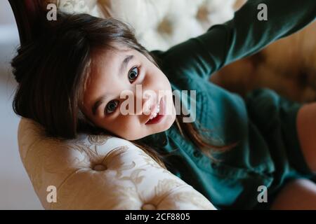 Grand angle de sourire enfant allongé sur un canapé confortable et se rafraîchir pendant le week-end tout en regardant la caméra Banque D'Images