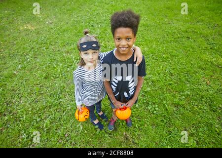 Portrait de deux enfants en costume d'Halloween embrassant et souriant à l'appareil photo tout en étant debout sur l'herbe verte à l'extérieur Banque D'Images
