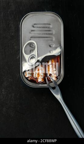 Vue de dessus de la composition des sardines en conserve et de la fourchette placée sur un panneau en ardoise sur fond noir Banque D'Images