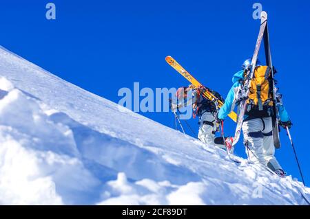 Les freeriders montent sur une colline abrupte lors d'une parfaite journée d'hiver Banque D'Images