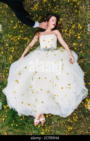Vue de dessus du marié caressant charmante mariée couché robe de mariage blanche décorée de pissenlits frais Banque D'Images