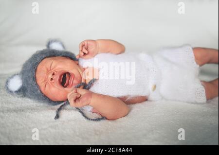 Mignon nouveau-né pleurs petit garçon dormant dans un lit de bébé dans un costume tricoté avec des oreilles. Modèle d'emballage pour bébés. Enfant en bonne santé, concept d'hôpital Banque D'Images