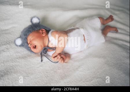 Mignon nouveau-né pleurs petit garçon dormant dans un lit de bébé dans un costume tricoté avec des oreilles. Modèle d'emballage pour bébés. Enfant en bonne santé, concept d'hôpital Banque D'Images