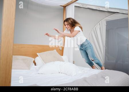 Bonne jeune femme tombant sur le lit avec du linge blanc dans une grande tente avec un toit transparent Banque D'Images