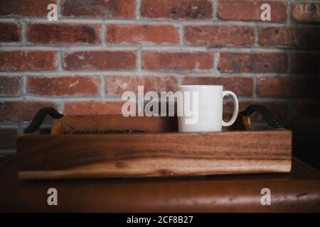 Valises brunes en cuir à l'ancienne avec tasse blanche en bois plateau près du mur de briques à plat Banque D'Images