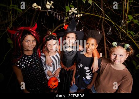 Groupe d'enfants heureux en costumes souriant à l'appareil photo et Célébrez Halloween ensemble dans la forêt sombre Banque D'Images