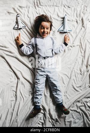 Vue de dessus d'un enfant souriant portant un espace allongé sur le lit avec des vaisseaux spatiaux et regarder la caméra Banque D'Images