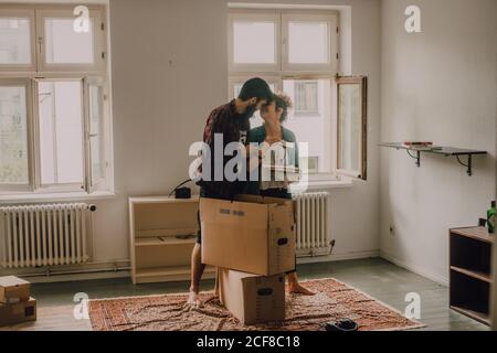 Hipster couple déballer les boîtes tout en se tenant pieds nus dans la lumière la chambre et les câlins Banque D'Images