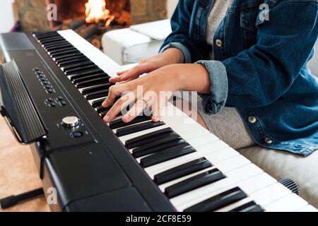 Crop femme en tenue décontractée assis sur un canapé jouant électrique piano tout en passant du temps à la maison Banque D'Images