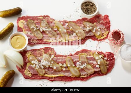 Préparation de roulades de viande allemande traditionnelle avec des bandes de bœuf maigre, bacon, cornichons, moutarde et épices dans un plat, couché sur blanc Banque D'Images