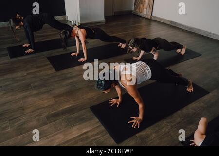 Des femmes pieds nus inreconnaissables dans les vêtements de sport se concentrant et faisant planche d'exercice sur les tapis de sport sur parquet contre blanc murs du hall spacieux Banque D'Images