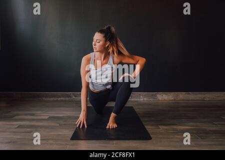 Grand angle de la femme confiante barefooted dans les vêtements de sport stretching body dans eka pada rajakapotasana deux positions sur le tapis et regarder loin tout en s'entraîner dans la salle d'entraînement moderne et spacieuse Banque D'Images