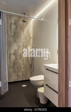 Intérieur clair et propre avec douche de plain-pied ouverte et rideau à côté des toilettes et du lavabo dans un petit confortable blanc et gris toilettes de l'hôtel Banque D'Images