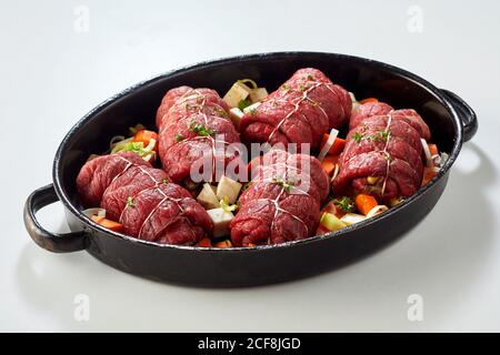 Plaque de cuisson avec roulades de bœuf non cuites et garnitures de légumes frais prêt à cuire sur fond blanc Banque D'Images