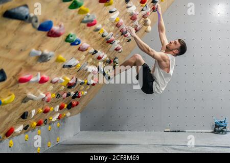 De la vue du côté doux de l'athlète masculin fort dans les vêtements de sport grimpez sur un mur coloré pendant l'entraînement dans un type moderne Banque D'Images