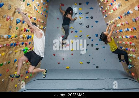 Vue latérale d'un jeune groupe de hommes et de femmes forts grimpeurs qui s'entraîne sur le mur dans la salle de gym moderne Banque D'Images