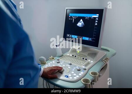 Grand angle de la personne de récolte dans l'uniforme médical en utilisant spécial équipement d'échographie lors de l'exécution du diagnostic de la maladie du patient à la lumière chambre de l'hôpital moderne Banque D'Images