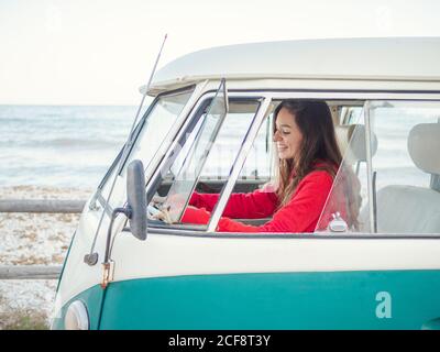 Vue latérale d'une jeune femme conduisant une fourgonnette vintage en bord de mer Banque D'Images