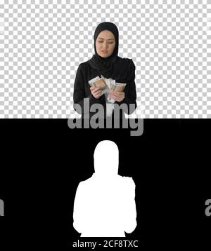 Jolie femme dans hijab marchant et comptant l'argent, Alpha Channel Banque D'Images