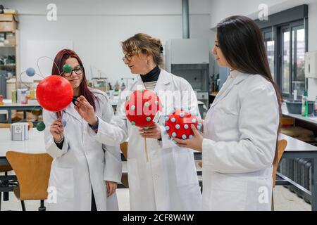 Femme mature en blouse de laboratoire examinant des modèles moléculaires de jeunes étudiantes pendant le travail en laboratoire moderne Banque D'Images