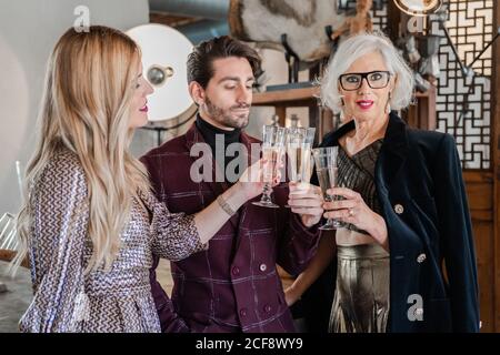 Femme âgée pensive en vêtements élégants et enfants adultes se félicitant mutuellement avec un événement familial tout en buvant du champagne ensemble à la maison Banque D'Images