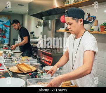 Des hommes multiraciaux cuisent des plats japonais dans un restaurant asiatique à l'intérieur Banque D'Images