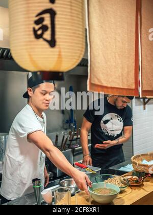Des hommes multiraciaux cuisent un plat japonais appelé ramen dans un restaurant asiatique intérieur Banque D'Images