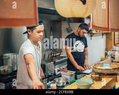 Des hommes multiraciaux cuisent des plats japonais dans un restaurant asiatique à l'intérieur Banque D'Images