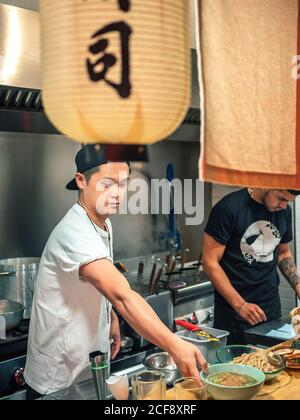 Des hommes multiraciaux cuisent un plat japonais appelé ramen dans un restaurant asiatique intérieur Banque D'Images