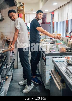Vue latérale de jeunes hommes multiraciaux qui cuisent un plat japonais appelé Ramen dans le restaurant asiatique et regarder la caméra Banque D'Images