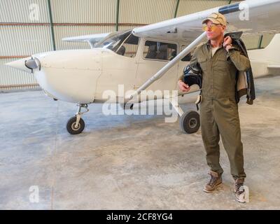 Pilote confiant à côté de l'avion rétro dans le hangar Banque D'Images
