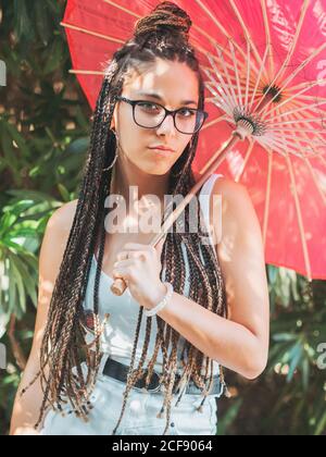 Belle petite femme mince en tenue d'été et avec parapluie debout jambes croisées près des arbres en fleurs Banque D'Images