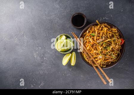 Pâtes végétariennes asiatiques, nouilles udon faites maison avec champignons shiitake sautés, sésame et légumes, sauce soja et citron vert, copie de fond gris foncé Banque D'Images