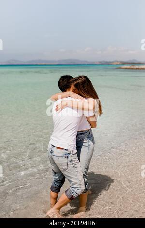 Vue arrière de l'homme et de la femme romantiques en tenue décontractée se tenant dans les eaux peu profondes de la côte tropicale en été Banque D'Images